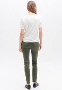 Camisa blanca de manga corta combinada con pantalones verdes ajustados. La camisa tiene un cuello redondo, mientras que los pantalones presentan un diseño slim y bolsillos mínimos.