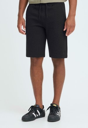 Zwarte shorts van gestructureerde stof, met een elastische tailleband met trekkoord. Gecombineerd met zwarte sneakers met witte accenten.