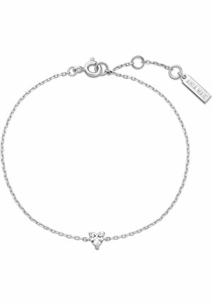 Bracciale delicato con catena in argento, con un piccolo centro in gemma trasparente a forma di cuore e una targhetta metallica con il marchio vicino alla chiusura.