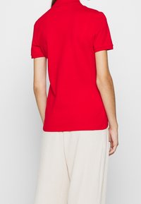 Rød polo skjorte med klassisk krave og korte ærmer, lavet af glat stof. Matchet med let beige vidde bukser.