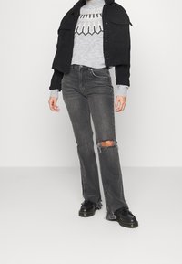 Chaqueta negra corta sobre un suéter de punto gris claro con un patrón geométrico, combinada con jeans grises desgastados y zapatos de plataforma negros.