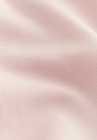 Weicher, hellrosa Stoff mit feiner Strickstruktur und sanften Falten, die subtile Schatten und Lichtreflexe erzeugen.