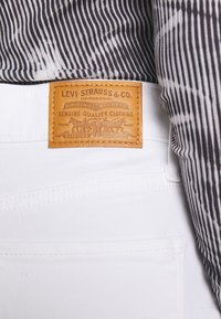 White denim jeans with a brown leather patch displaying "Levi Strauss & Co." and striped fabric visible above the waistband.