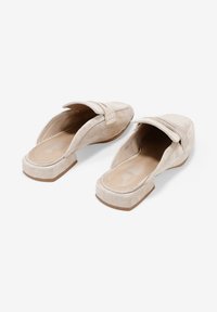Zapatos de ante beige tipo slip-on con puntera cuadrada, tacón bajo y bloque, y un detalle decorativo de costura en la parte superior. Forro interior suave.