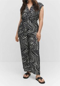 Mono a rayas blanco y negro con mangas cortas, que presenta un diseño de frente cruzado, cintura ceñida con cinturón y piernas anchas. Llevado con sandalias negras.