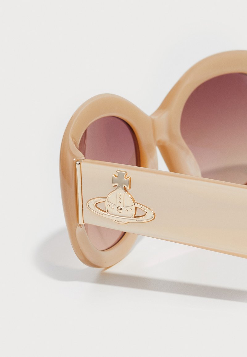 Peachfarvede solbriller med runde linser, der har et guld planetlogo på stangen. Materialet har en blank finish og en glat tekstur.