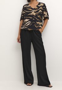 Haut léger bleu marine avec des motifs ondulés dorés et beiges, associé à un pantalon noir à jambes larges. Les deux articles ont une coupe décontractée et une texture douce.