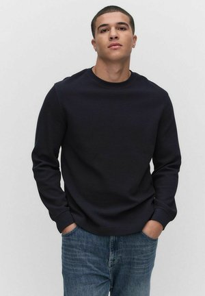 Sweat-shirt à manches longues bleu marine avec un motif texturé, col rond et poignets côtelés, assorti à un jean en denim bleu clair.