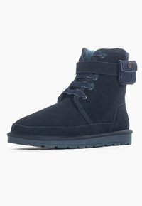 Botas de tobillo de ante azul oscuro con punta redonda, cierre con cordones y una correa de tela. Presentan una suela texturada para mayor agarre y una pestaña de acento de denim.