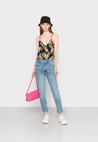 Bodysuit preto com padrão floral e alças finas, jeans azul claro com folhos, ténis brancos e uma mala texturizada rosa. Acento de chapéu de balde.