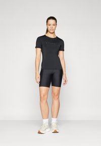 Black athletic top with short sleeves, featuring a subtle logo; paired with black bike shorts, showcasing a sleek fit and smooth texture.