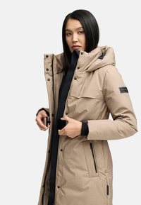 Beige polstret frakke med hætte, der har en frontlynlås, trykknapper og sidelommer. Struktureret stof og logoaccent på ærmet.