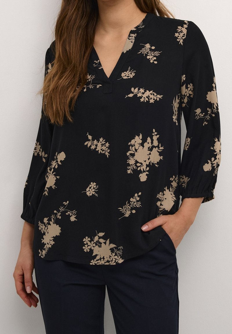 Blusa negra con escote en V, que presenta patrones florales en color beige, mangas tres cuartos y un corte relajado. El material parece suave y liso.