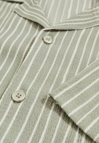 Hellgrünes gestreiftes Hemd aus strukturiertem Stoff, mit Kragen und silbernen Knöpfen im Vierloch-Design, akzentuiert durch weiße Streifen.
