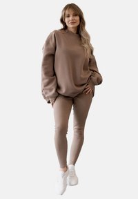 Brązowy, oversize'owy sweter z ribbowymi mankietami, w połączeniu z dopasowanyymi legginsami. Białe trampki dopełniają stylizację. Miękka, teksturowana tkanina.