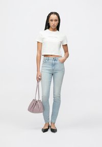 Camiseta blanca corta, jeans ajustados azul claro, bailarinas negras y bolso de mano lavanda con cordón. Tela suave con un diseño sencillo.