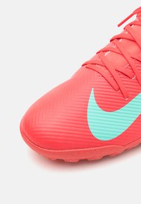 Scarpa da calcio rossa brillante con upper texturizzato, caratterizzata da un grande swoosh Nike turchese, punta rinforzata e numerosi tacchetti sulla suola.
