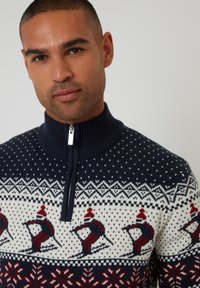 Maglione zip-up navy con colletto a costine, caratterizzato da motivi di sci bianchi e rossi e motivi di fiocchi di neve su un design a maglia texturizzata.