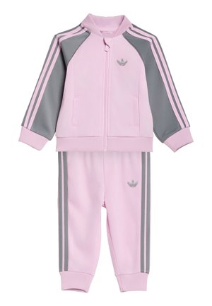 Tuta Adidas rosa e grigia per bambini piccoli con giacca con zip, tasche laterali, polsini a costine e pantaloni abbinati con strisce laterali.