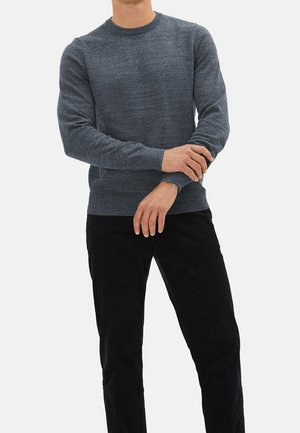 Grauer Rundhalsausschnittpullover mit strukturiertem Finish, langen Ärmeln und gerippten Bündchen, kombiniert mit schwarzen Hosen, steht vor einem weißen Hintergrund.