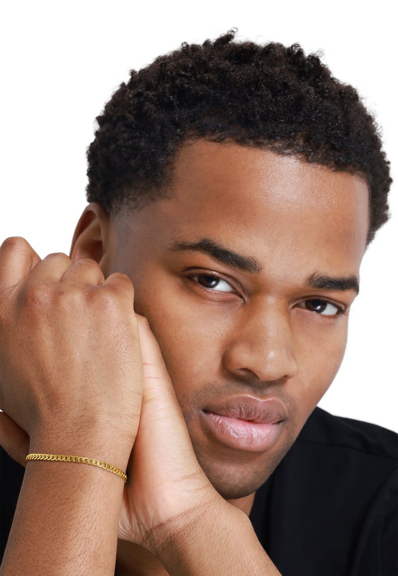 Goldene Kettenarmband an einem Handgelenk, mit verbundenen Gliedern; die Hände des Modells miteinander verwoben, mit sichtbarer Hautstruktur, vor einem weißen Hintergrund.