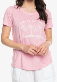 Lyserød kortærmet t-shirt med rund halsudskæring og et hvidt palmetræ-grafik med teksten “SUNSET ESCAPE Roxy” nedenfor. Blødt og let stof.