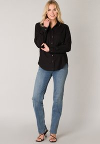 Zwarte overhemd met lange mouwen en een borstzak, gecombineerd met lichtblauwe jeans en zwarte haksandalen. Eenvoudig ontwerp en pasvorm.