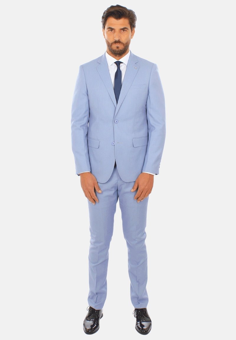 Abito azzurro chiaro con una vestibilità su misura, caratterizzato da una chiusura a due bottoni, rever a punta e pantaloni con frontale piatto. Indossato con una camicia bianca e una cravatta blu navy.