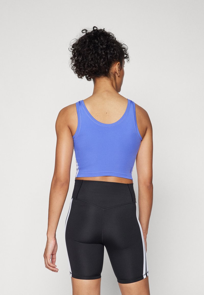 Top corto azul combinado con pantalones cortos negros de tiro alto que cuentan con franjas laterales blancas, mostrando un diseño ajustado y una textura suave.