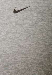 Šedé sportovní tričko s texturovaným vzorem a černým logem Nike Swoosh v horní levé části.