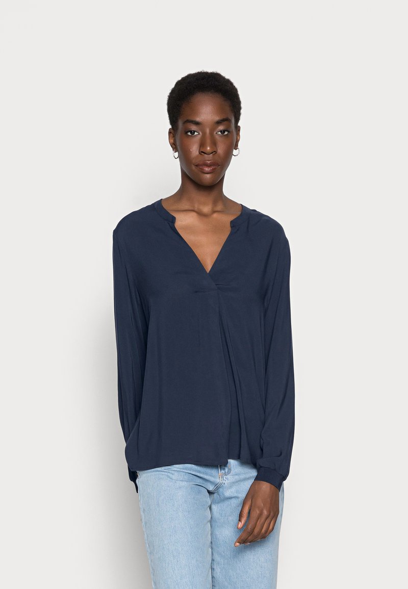 Blusa de manga longa azul marinho com decote em V, corte descontraído e detalhes de pregas subtil. Tecido leve com uma textura suave.