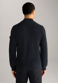 Dunkelblauer Strickpullover mit Rippstruktur und langen Ärmeln, ausgestattet mit einem umgeschlagenen Kragen und einem dezenten Logodetail am Ärmel.