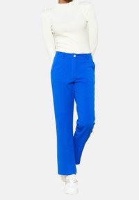 Blå skräddarsydda byxor i mjukt tyg med knappstängning och hällor för bälte. Bärs med en figursydd vit ribbad topp och vita sneakers.