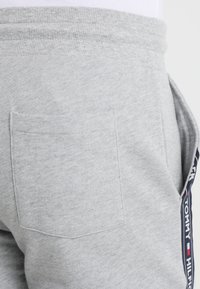 Pantalones de chándal grises de algodón con un bolsillo trasero y una franja lateral con el logotipo de la marca en colores azul marino, rojo y blanco. Textura suave.
