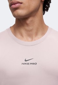 Gros plan d'une personne portant un t-shirt Nike Pro rose clair avec un logo Nike noir centré sur la poitrine.