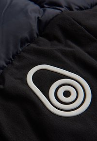 Svart tyg med en slät textur pryds av en vit gummiklogotyp som består av koncentriska cirklar och en omslutande form.