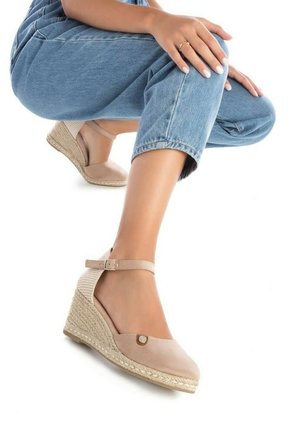Espadrille de cuña beige con correa en el tobillo, textura tejida, caja de dedos plana, detalle de botón decorativo, sobre un fondo blanco.