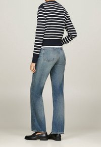 Maglione a righe navy e bianche con orlo a coste, abbinato a jeans blu a gamba dritta. Mocassini neri completano l'outfit.