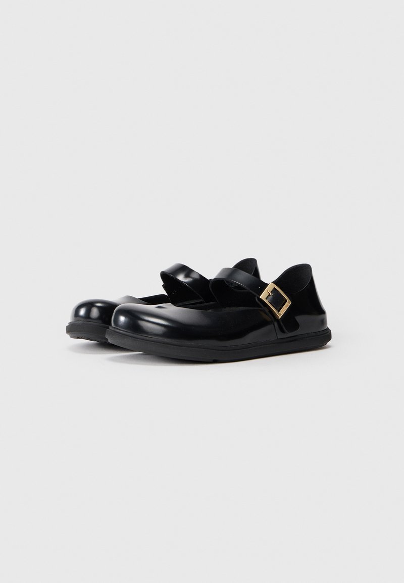 Zapatos de goma negros con dos correas anchas y un acento de hebilla dorada. Punta redondeada y un interior texturizado negro. Suela plana de goma.