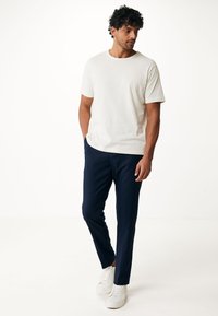 Vit kortärmad t-shirt med subtil textur; kombinerad med marinblå byxor och vita sneakers, som visar upp en avslappnad, modern outfit.
