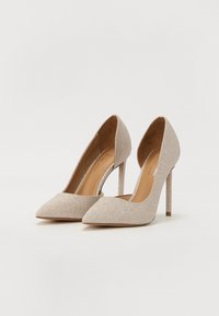 Tacchi alti champagne brillanti con punta affilata, tacco a stiletto e design aperto sul retro. Texture liscia con una leggera lucentezza.