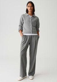 Cardigan gris à côtes avec un col et une poche poitrine, associé à un pantalon plissé gris et des baskets blanches.