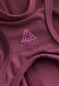 Gros plan sur un tissu de sport marron rouge avec des bords cousus et un logo rose comportant des lignes triangulaires et le mot « ACTIVE ».