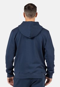 Marineblauer Kapuzenpullover aus weichem Stoff, mit einer vorderen Tasche, langen Ärmeln und einer geräumigen Kapuze mit glatter Textur sowie gerippten Bündchen.