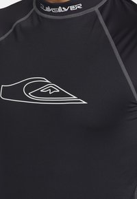 Černý rash guard vyrobený z elastického materiálu, s bílým logem Quiksilver na přední straně. Obsahuje šedé švy podél švů.
