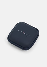 Estuche azul marino con cremallera y textura suave, con un logo blanco "TOMMY HILFIGER" centrado en el frente. Diseño cuadrado compacto.
