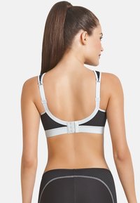 Black sports bra with mesh texture, silver accents, adjustable straps, and a hook-and-eye closure at the back.