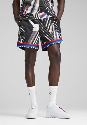 Schwarze Sportshorts mit geometrischem Muster, versehen mit roten und blauen Akzenten, kombiniert mit weißen Socken und weißen Turnschuhen.