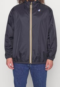 Giacca leggera nera in nylon. Presenta un colletto alto, polsini elastici e una zip frontale con strisce gialle e bianche. Logo del marchio sul petto.