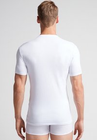 Biała, krótko rękawowa koszulka bawełniana z okrągłym dekoltem, dopasowany krój i gładka faktura, noszona z pasującymi białymi slipami.